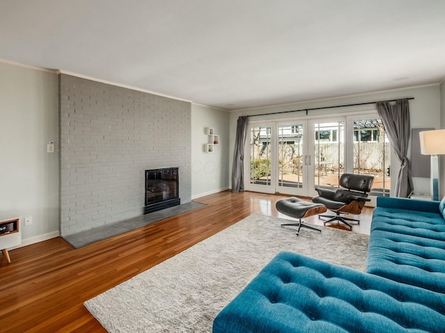 living area with crown molding, a brick fireplace, wood finished floors, and baseboards