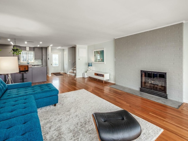 living area featuring a fireplace, stairs, baseboards, and wood finished floors