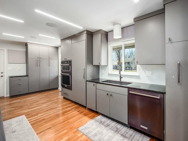 kitchen featuring stainless steel dishwasher, dark countertops, gray cabinets, and a sink