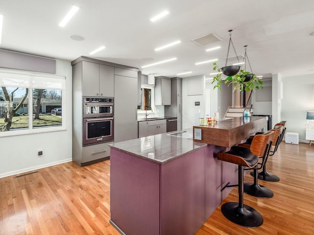 kitchen featuring double oven, a breakfast bar area, gray cabinets, light wood-style flooring, and a sink