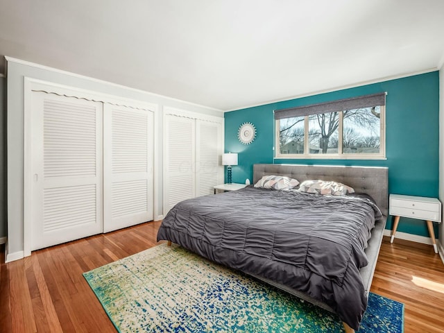 bedroom with baseboards, multiple closets, and wood finished floors