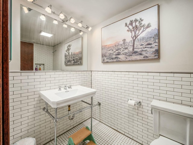 half bathroom featuring a sink, a wainscoted wall, toilet, and tile walls