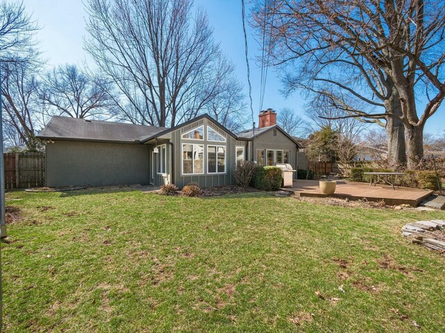 rear view of house with board and batten siding, fence, a chimney, a deck, and a yard