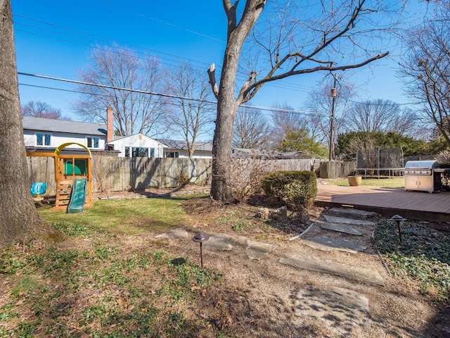 view of yard featuring a deck, a playground, a trampoline, and a fenced backyard