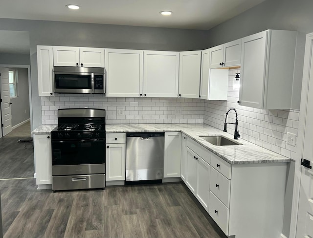 kitchen featuring a sink, white cabinets, appliances with stainless steel finishes, light stone countertops, and dark wood finished floors