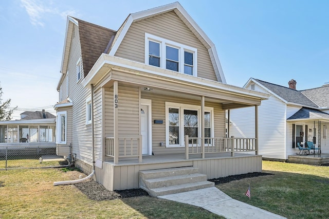 colonial inspired home with a gambrel roof, a front lawn, a porch, fence, and roof with shingles