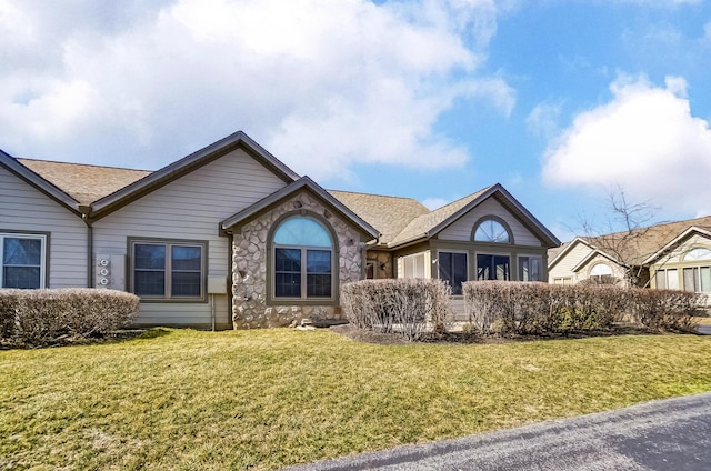 single story home with stone siding, a front lawn, and roof with shingles