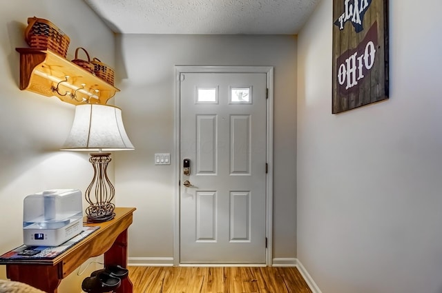 foyer with baseboards, a textured ceiling, and wood finished floors