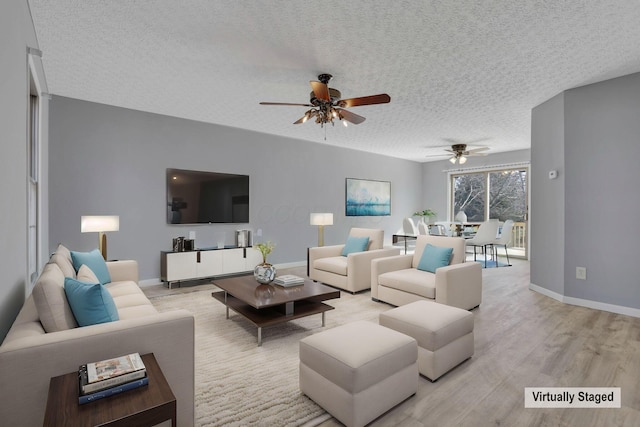 living room with a ceiling fan, light wood-style floors, baseboards, and a textured ceiling