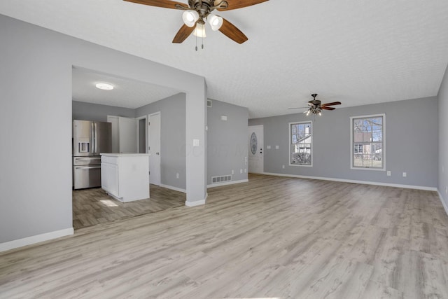 unfurnished living room featuring light wood finished floors, visible vents, a textured ceiling, and baseboards