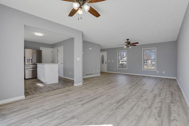 unfurnished living room with baseboards, visible vents, light wood-style flooring, ceiling fan, and a textured ceiling