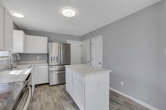 kitchen featuring light wood-style flooring, a sink, white cabinetry, stainless steel fridge, and light countertops