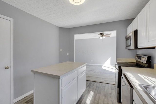 kitchen with appliances with stainless steel finishes, light wood-style flooring, a ceiling fan, and white cabinetry