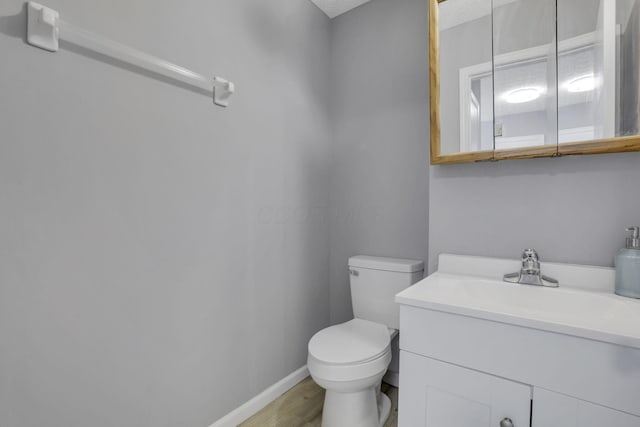 half bath featuring vanity, toilet, wood finished floors, and baseboards