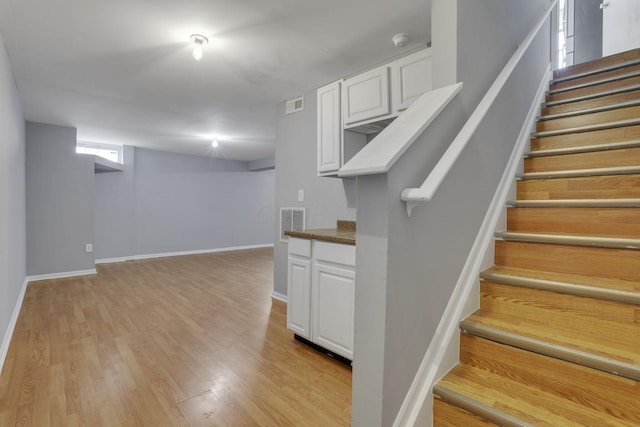 stairway with visible vents, baseboards, and wood finished floors