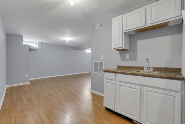 kitchen featuring dark countertops, visible vents, light wood-style flooring, and a sink