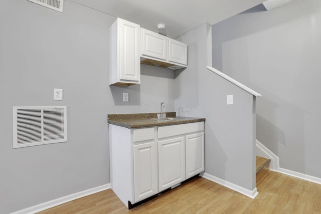 kitchen featuring visible vents, light wood-style flooring, white cabinets, and a sink