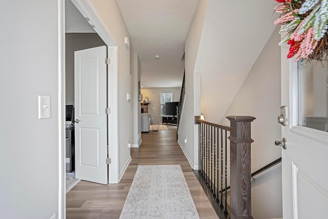 corridor with wood finished floors, an upstairs landing, and baseboards