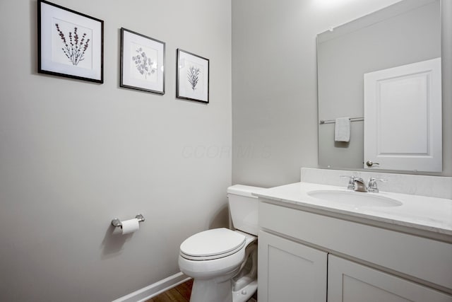 half bath with baseboards, toilet, wood finished floors, and vanity