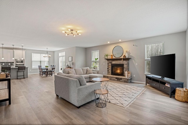 living area featuring a stone fireplace, a textured ceiling, light wood-style floors, and a chandelier