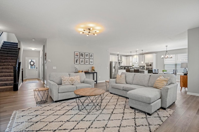 living room featuring stairway, baseboards, a notable chandelier, and wood finished floors