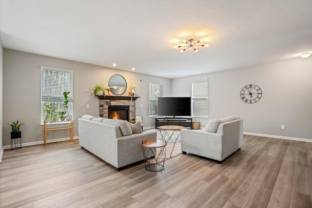 living room with baseboards, a chandelier, light wood-type flooring, a stone fireplace, and a textured ceiling