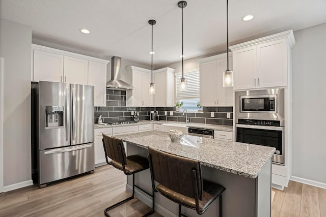 kitchen with light wood-style flooring, white cabinets, appliances with stainless steel finishes, wall chimney exhaust hood, and tasteful backsplash