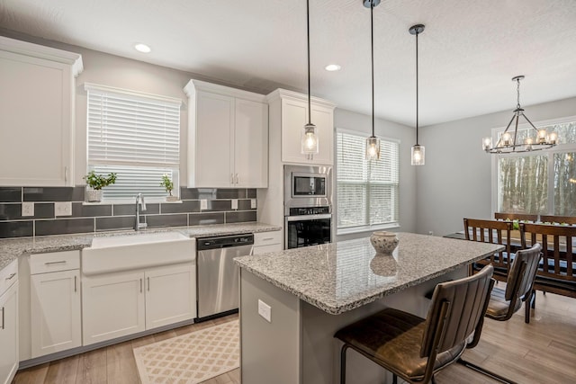 kitchen with a kitchen island, decorative backsplash, white cabinets, stainless steel appliances, and a sink