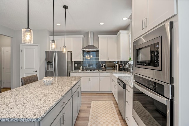 kitchen with a sink, a kitchen island, appliances with stainless steel finishes, wall chimney range hood, and decorative backsplash