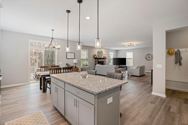 kitchen featuring decorative light fixtures, light wood-type flooring, a stone fireplace, and a center island