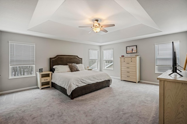 bedroom with light carpet, multiple windows, a raised ceiling, and baseboards