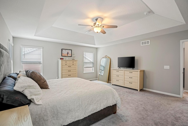 bedroom featuring visible vents, baseboards, light carpet, a raised ceiling, and a ceiling fan