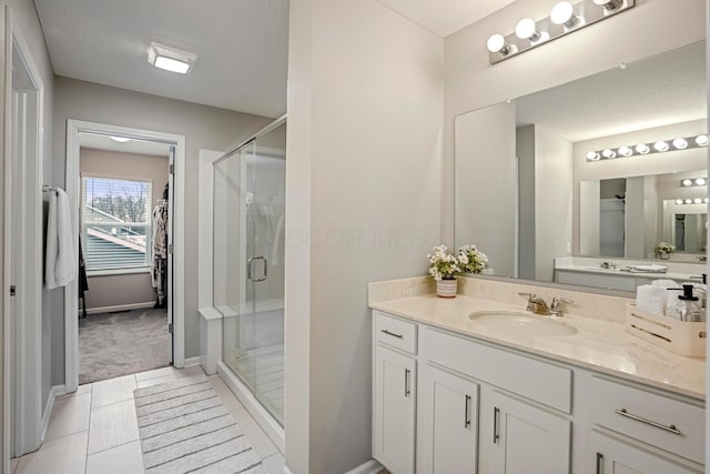 bathroom with a spacious closet, a shower stall, baseboards, tile patterned floors, and vanity