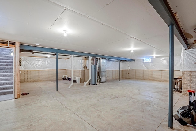 basement featuring water heater, brick wall, and stairs