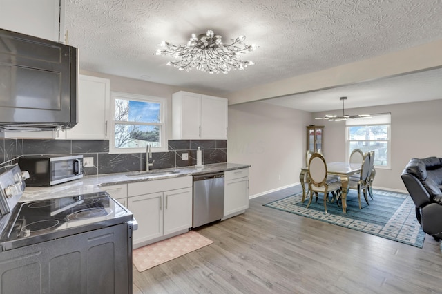 kitchen featuring light wood finished floors, stainless steel appliances, backsplash, white cabinets, and a sink