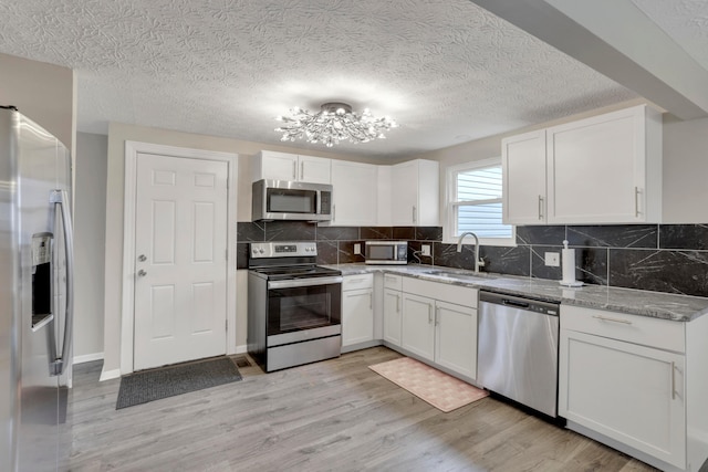 kitchen with light stone counters, stainless steel appliances, a sink, white cabinetry, and light wood finished floors