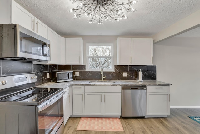 kitchen with appliances with stainless steel finishes, light wood-type flooring, white cabinetry, and a sink