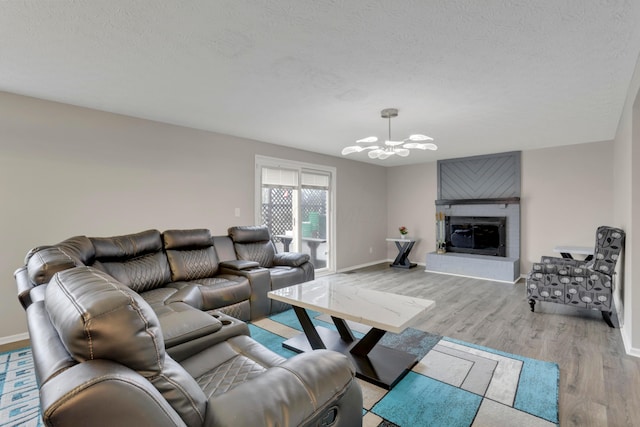 living room with light wood finished floors, a textured ceiling, a notable chandelier, and a glass covered fireplace