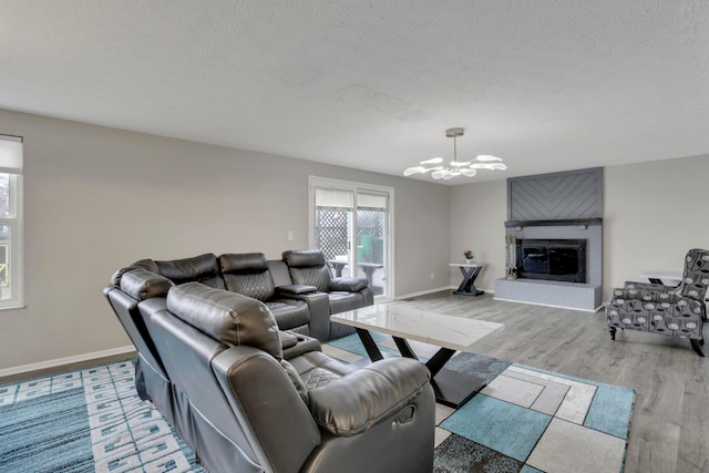 living room featuring a glass covered fireplace, a textured ceiling, light wood finished floors, and an inviting chandelier