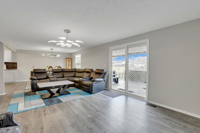 living area featuring a chandelier, a textured ceiling, baseboards, and wood finished floors