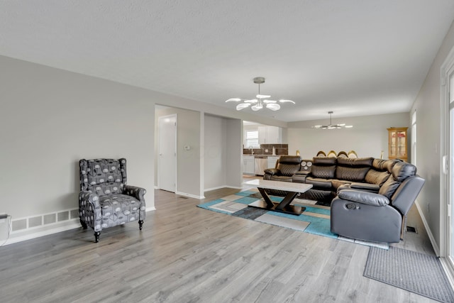 living room with a chandelier, visible vents, baseboards, and wood finished floors