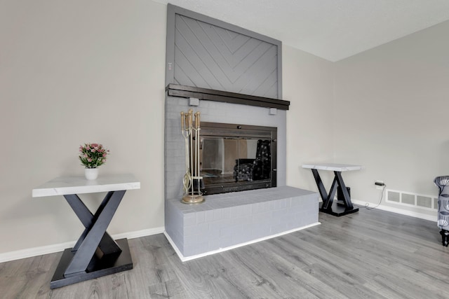 interior details with a brick fireplace, wood finished floors, visible vents, and baseboards