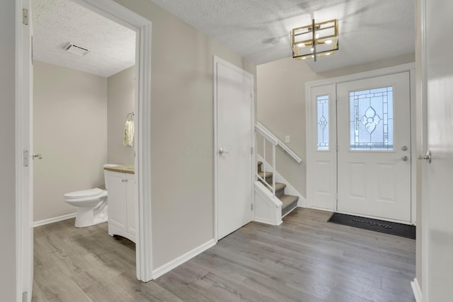 entrance foyer featuring light wood-type flooring, stairs, visible vents, and a textured ceiling