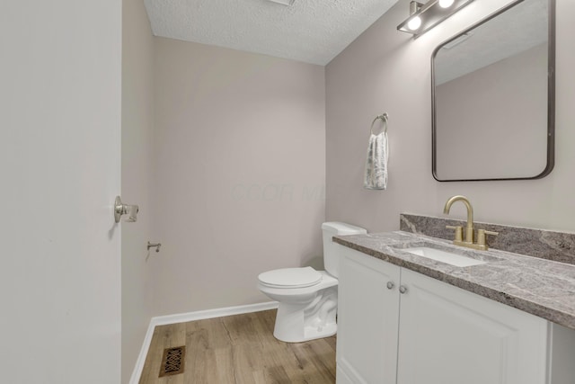 bathroom with a textured ceiling, toilet, wood finished floors, vanity, and visible vents