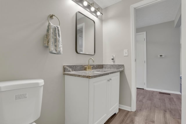 half bath with visible vents, toilet, vanity, wood finished floors, and baseboards