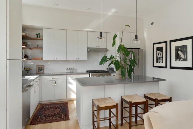 kitchen featuring under cabinet range hood, white cabinetry, appliances with stainless steel finishes, and a kitchen breakfast bar