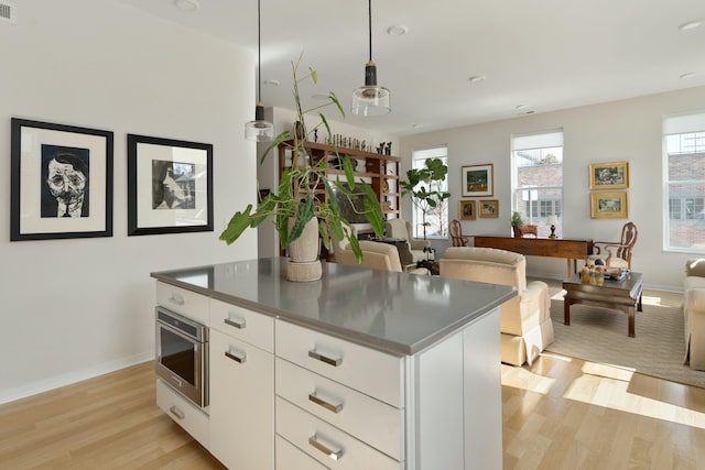 kitchen featuring a kitchen island, white cabinets, light wood-style floors, stainless steel counters, and modern cabinets