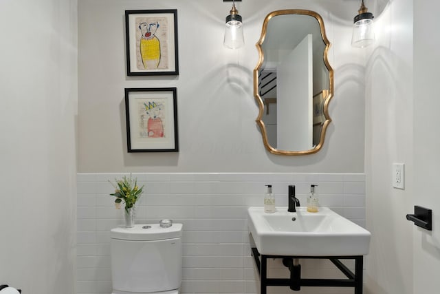 half bathroom with a wainscoted wall, a sink, tile walls, and toilet