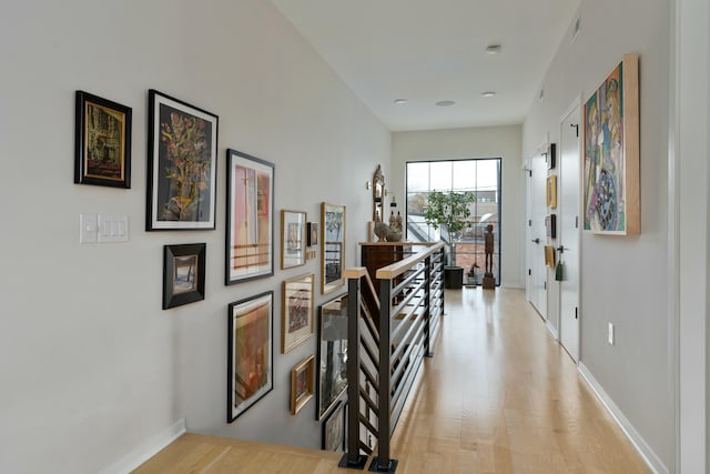 hallway with light wood-type flooring, visible vents, baseboards, and an upstairs landing