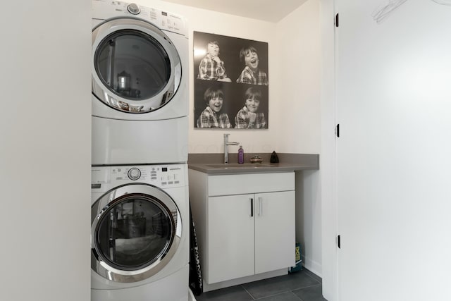 laundry area with cabinet space, dark tile patterned flooring, a sink, and stacked washer and clothes dryer